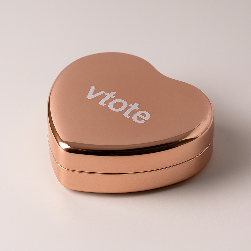 Bálsamo labial em formato de coração dourado rosa com gravação “Vtote”, acabamento metálico brilhante e tampa de pressão, fotografado em fundo neutro de estúdio.