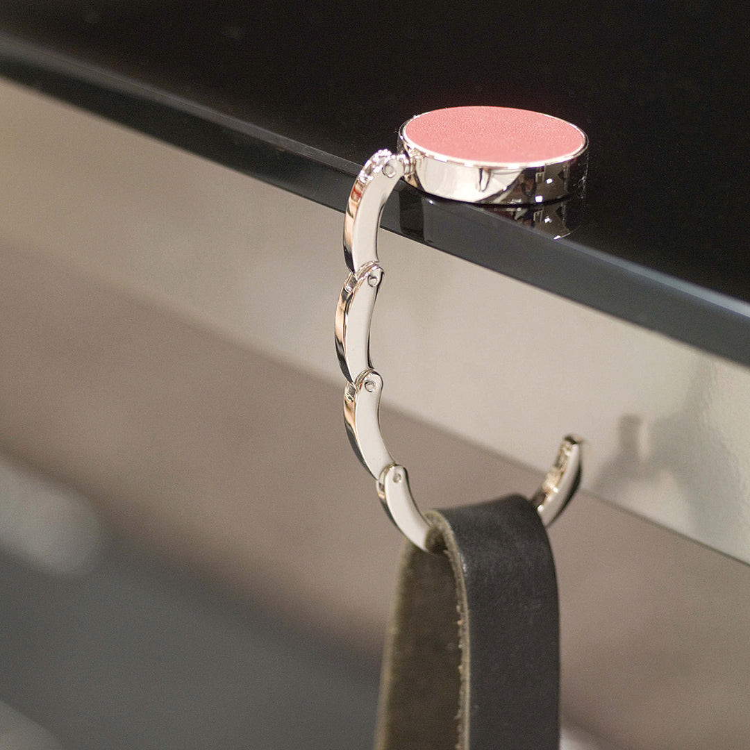 Cabide dobrável de metal com acabamento prateado e topo em couro PU castanho escuro, com gravação laser “Vtote”, segurando uma mala em mesa de restaurante moderna.