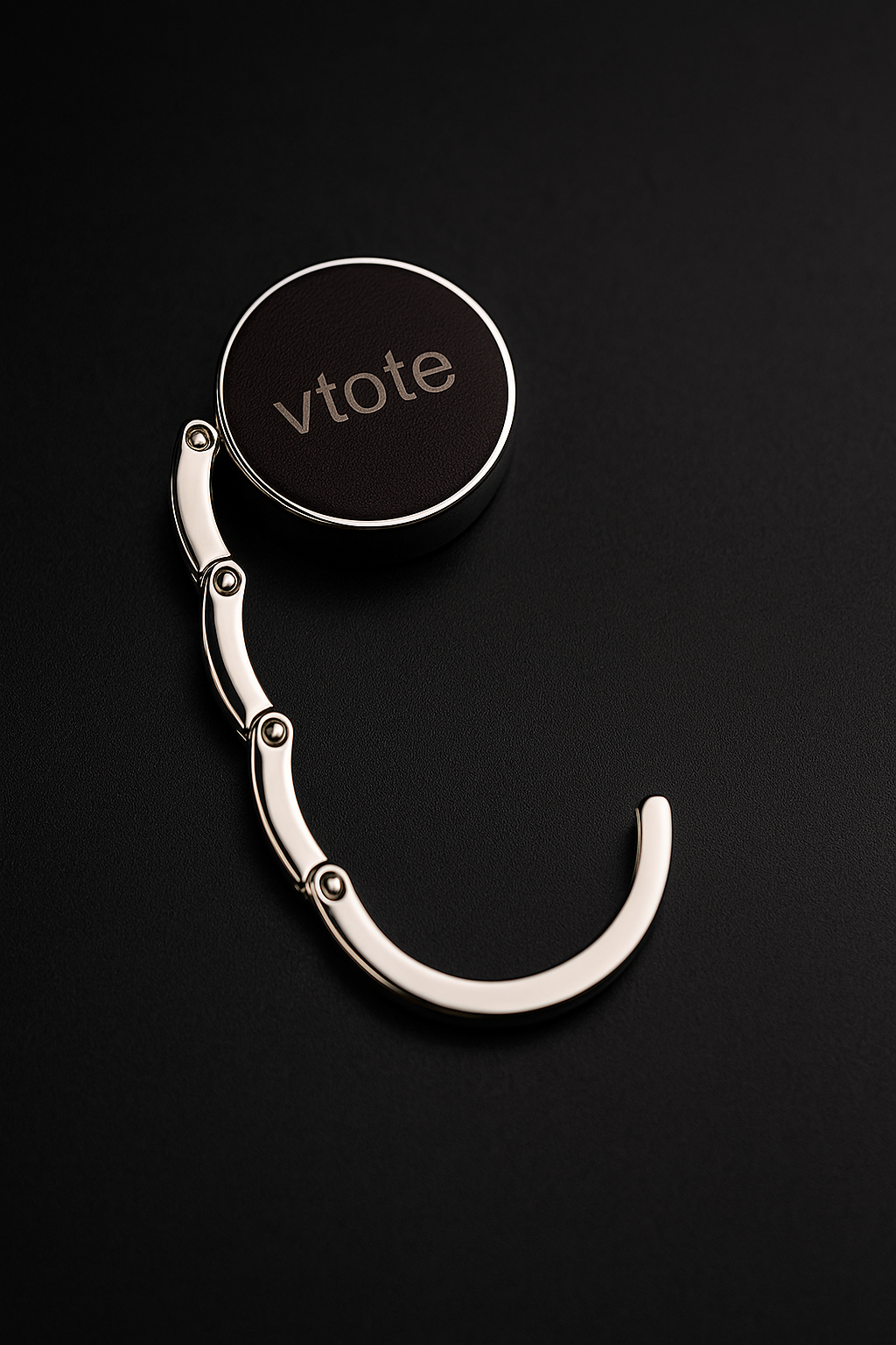 Cabide dobrável de metal com acabamento prateado e topo em couro PU castanho escuro, com gravação laser “Vtote”, segurando uma mala em mesa de restaurante moderna.