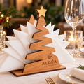 Porta-guardanapos de Natal em madeira em formato de árvore com estrela dourada, personalizado com o logótipo ALDÊA Restaurante através de gravação laser, com guardanapos brancos numa mesa decorada para o Natal.
